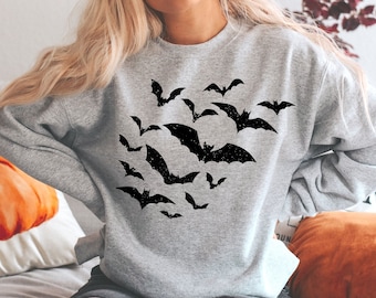 May include: A light grey crewneck sweatshirt featuring a black graphic print of a swarm of bats in flight. The bats are depicted in various sizes and positions across the centre of the chest, creating a cluster effect with a distressed texture.