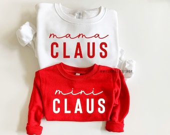 Könnte beinhalten: Zwei Weihnachts-Sweatshirts. Ein weißes Sweatshirt mit rotem Text, der "mama claus" sagt, und ein rotes Sweatshirt mit weißem Text, der "mini claus" sagt.
