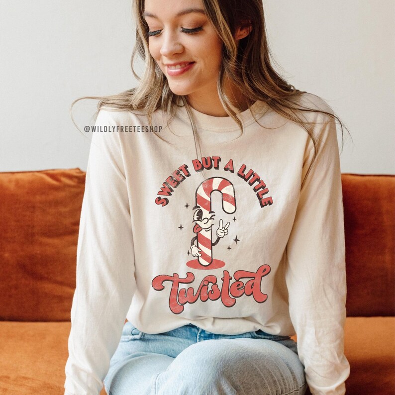 May include: A white long-sleeved shirt with a red and white candy cane graphic and the text "Sweet but a little twisted".
