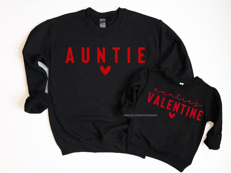 Może przedstawiać: Dwie czarne bluzy z czerwonym nadrukiem. Większa bluza ma napis "AUNTIE" z czerwonym sercem. Mniejsza bluza ma napis "auntie's VALENTINE" z czerwonym sercem.