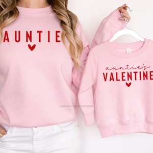 Może przedstawiać: R&oacute;żowe bluzy z czerwonym nadrukiem. Większa bluza ma napis "AUNTIE" z sercem. Mniejsza bluza ma napis "auntie's VALENTINE" z sercem.