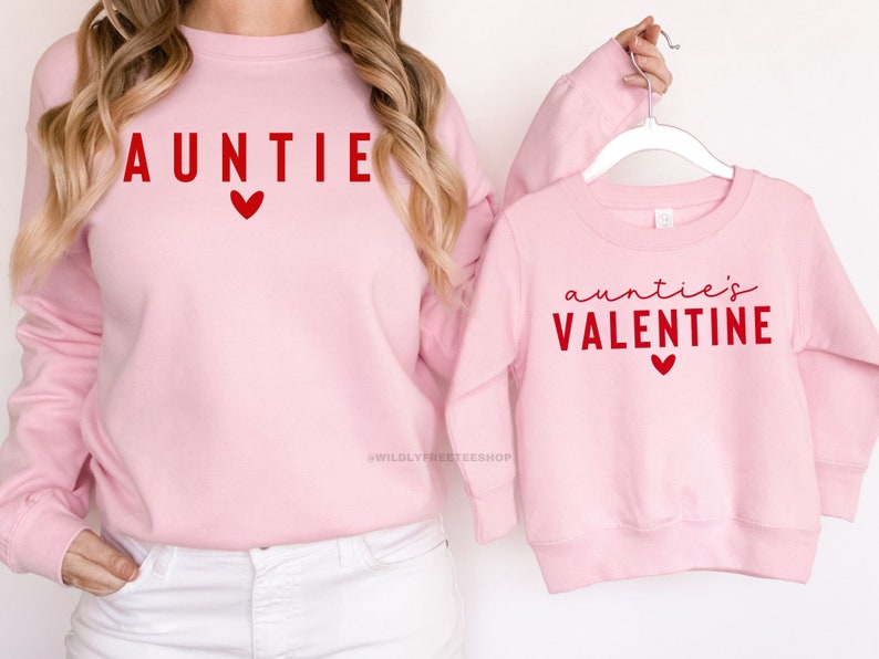 Może przedstawiać: R&oacute;żowe bluzy z czerwonym nadrukiem. Większa bluza ma napis "AUNTIE" z sercem. Mniejsza bluza ma napis "auntie's VALENTINE" z sercem.