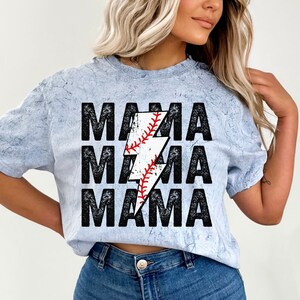 May include: A light blue t-shirt with a distressed look featuring the text "MAMA" repeated three times with a lightning bolt graphic in the centre. The lightning bolt is filled with a baseball graphic.