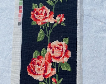 May include: Needlepoint canvas featuring a floral design of red and pink roses with green leaves on a black background. The needlepoint is on a white canvas with a color palette swatch on the left side.