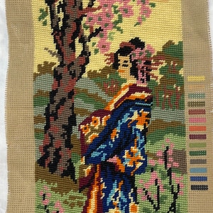 May include: Needlepoint tapestry depicting a geisha in a blue kimono, near a cherry blossom tree. The artwork is set against a yellow background with green and brown foliage. The text "ROYAL PARIS" is at the top.