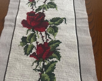 May include: Needlepoint canvas featuring a detailed design of red roses with green leaves and stems. The roses are in various stages of bloom, set against a light gray background. The canvas has a dark border.