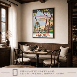 May include: A framed vintage travel poster for Cannes, France, featuring a coastal landscape with palm trees and the text "Cannes Cote D'Azur". The poster hangs above a small table set for tea, with chairs and a built-in bench.