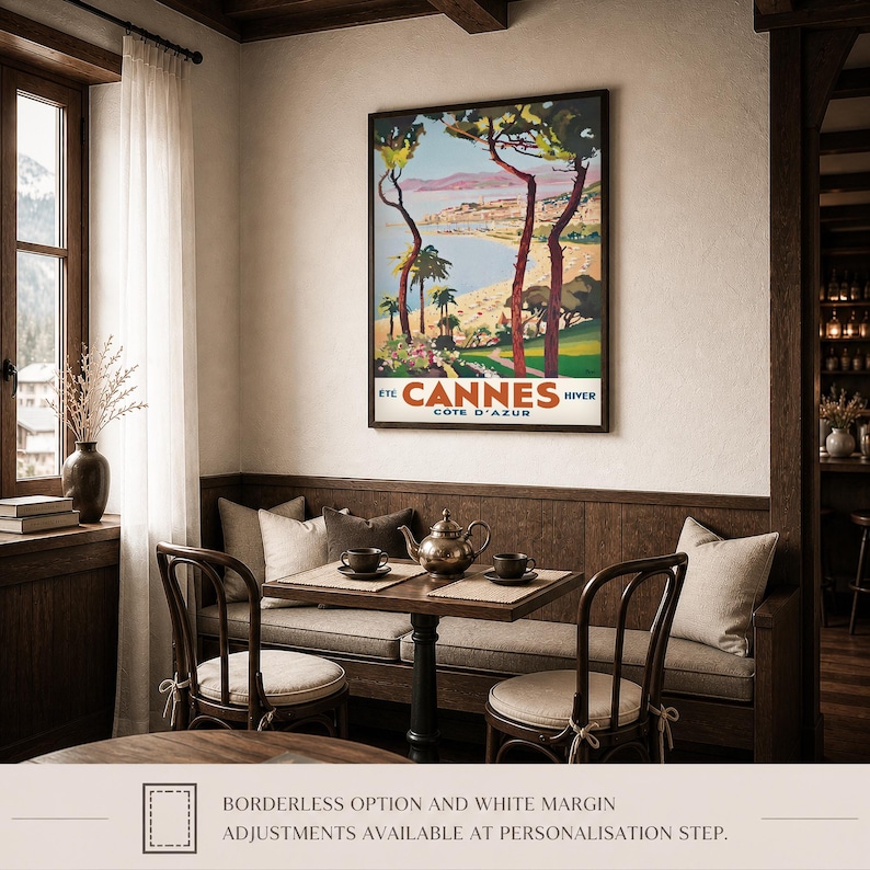May include: A framed vintage travel poster for Cannes, France, featuring a coastal landscape with palm trees and the text "Cannes Cote D'Azur". The poster hangs above a small table set for tea, with chairs and a built-in bench.