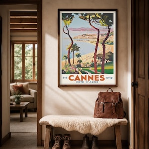 May include: A framed vintage travel poster for Cannes, France, hangs above a bench with a sheepskin throw. A brown leather backpack sits on the bench. The poster features a beach scene with palm trees and the text "Cannes C&ocirc;te d'Azur".