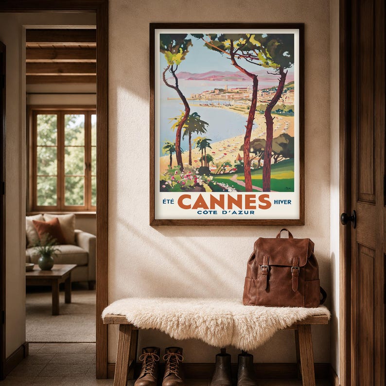 May include: A framed vintage travel poster for Cannes, France, hangs above a bench with a sheepskin throw. A brown leather backpack sits on the bench. The poster features a beach scene with palm trees and the text "Cannes C&ocirc;te d'Azur".