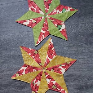 Könnte beinhalten: Zwei handgefertigte sternförmige Stoffornamente. Eines hat grüne und poinsettia-gemusterte Segmente, das andere goldene und poinsettia-gemusterte Segmente. Geeignet für festliche oder saisonale Dekoration.