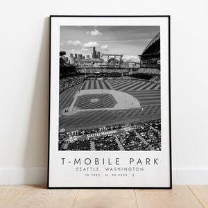 May include: Black and white photograph of T-Mobile Park, a baseball stadium in Seattle, Washington. The photo shows the field, the stands, and the city skyline in the background. The text "T-Mobile Park" is printed below the image, along with the address "Seattle, Washington 47.5983 N, 122.3321 W".