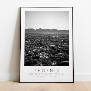 May include: Black and white photograph of Phoenix, Arizona, USA. The image shows a panoramic view of the city with mountains in the background. The text "PHOENIX", "UNITED STATES OF AMERICA", and "33.5722°N 112.0901°W" is printed below the image.