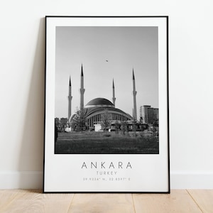 May include: Black and white photograph of a mosque in Ankara, Turkey. The mosque has a large dome and four minarets. The text "ANKARA TURKEY 39.9334° N, 32.8597° E" is printed below the image.