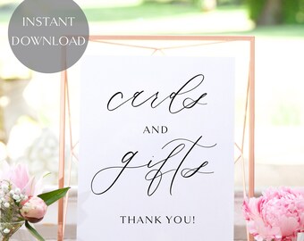 May include: A white sign with black calligraphy that reads "cards and gifts" with the words "Thank You!" at the bottom. The sign is in a gold metal frame.