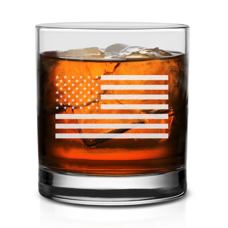 Puede incluir: Un vaso de vidrio transparente con un dise&ntilde;o de bandera estadounidense esmerilado. El vaso est&aacute; lleno de l&iacute;quido &aacute;mbar y cubitos de hielo.