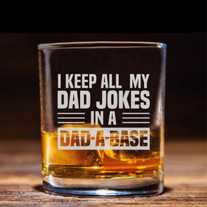 May include: A clear glass with a humorous saying etched on the side. The text reads "I keep all my dad jokes in a dad-a-base". The glass is filled with amber liquid and ice cubes.