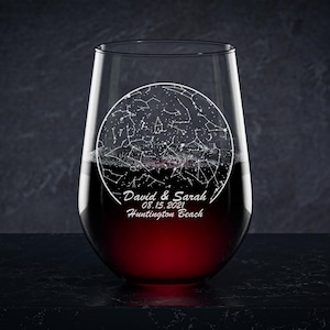 May include: A clear glass wine glass with a stem and a round base. The glass is engraved with a constellation map and the text "David & Sarah 03.15.2021 Huntington Beach".