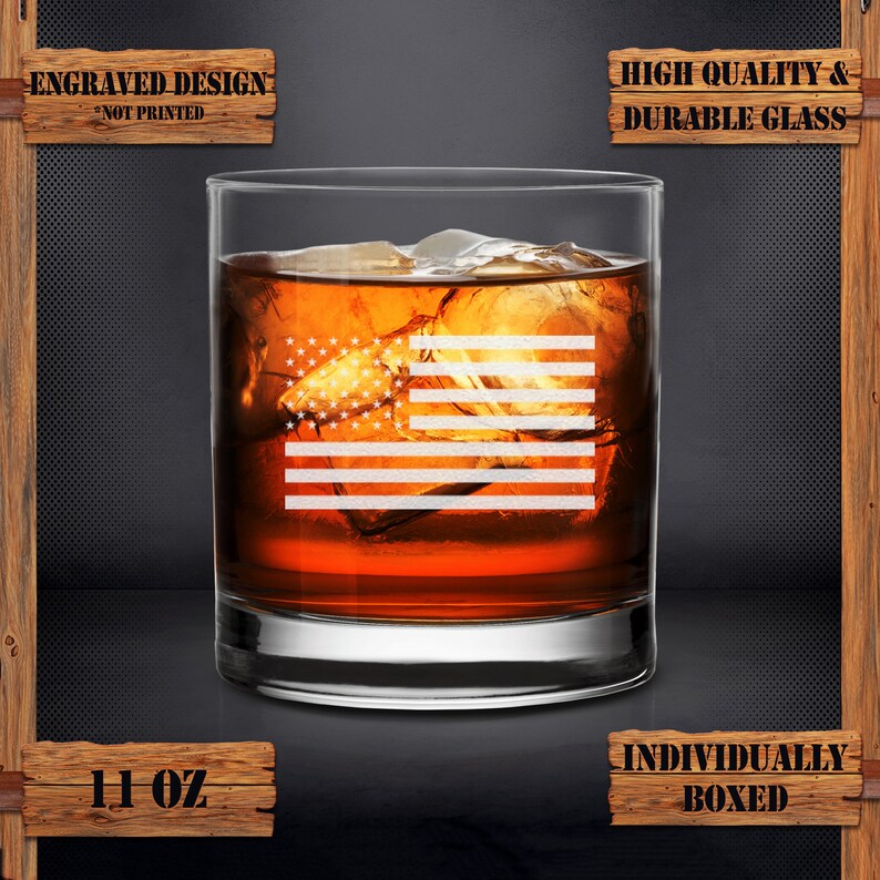Puede incluir: Un vaso de whisky de vidrio de 11 onzas con un dise&ntilde;o de bandera estadounidense grabado. El vaso est&aacute; lleno de l&iacute;quido &aacute;mbar y cubitos de hielo. El texto "Engraved Design - Not Printed" y "High Quality & Durable Glass" est&aacute;n en letreros de madera por encima y por debajo del vaso. El texto "Individually Boxed" est&aacute; en un letrero de madera debajo del vaso.