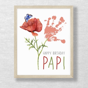 May include: A framed print featuring a watercolor illustration. A red poppy with a blue butterfly sits atop a green stem. A handprint and the words "HAPPY BIRTHDAY PAPI" are also included.