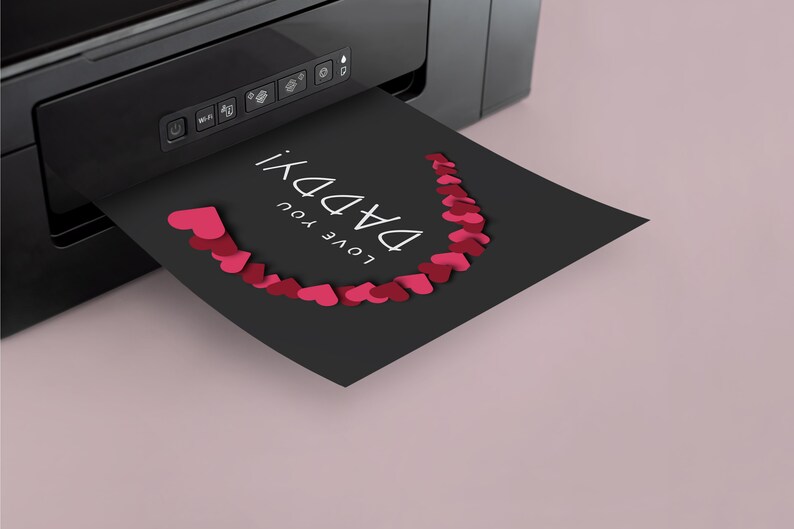 May include: A black card with the text "LOVE YOU DADDY" printed in white with a row of red paper hearts forming a semi-circle around the text. The card is being printed from a black printer.