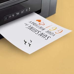 May include: A white card with the text "SUNSHINE your birthday 6!" printed on it is being printed from a black printer. The card has two red hearts and a rainbow-colored "6" on it.