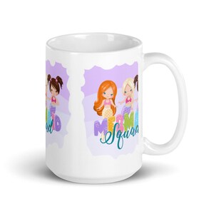Puede incluir: Taza de cer&aacute;mica blanca con un dise&ntilde;o morado y blanco con tres sirenas de dibujos animados con el texto "Mermaid Squad" en turquesa.