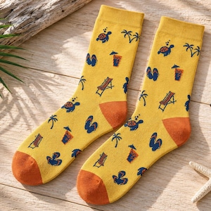 May include: A pair of yellow crew socks featuring a repeating pattern of dark blue sea turtles, palm trees, flip-flops, beach chairs, and orange tropical drinks with umbrellas. The socks have solid orange heels and toe sections.