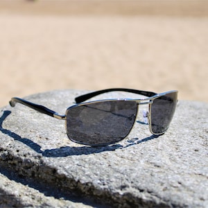 May include: Silver aviator sunglasses with dark gray lenses, resting on a gray rock.