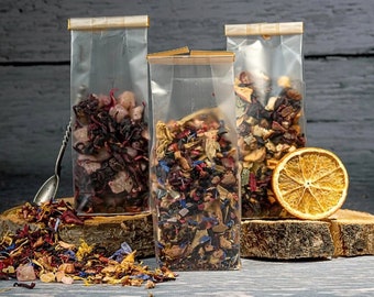 May include: Three clear plastic pouches filled with different types of dried fruit and flower tea blends. The pouches are sealed with gold tape and are sitting on a wooden surface.