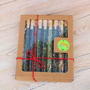 May include: A brown cardboard box with a clear window, containing a variety of tea samples in glass tubes with cork tops. The box is tied with a red ribbon and has a green and yellow sticker that says "Merry Christmas".