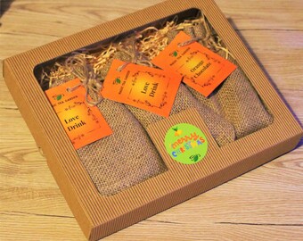 May include: A brown cardboard box with a clear window, containing four small hessian bags with orange and white labels. The labels read "Love Drink" and "Orange Chocolate". A green circle sticker with the text "merry christmas" is on the box.