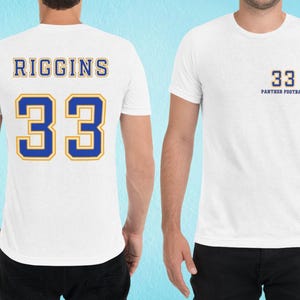 May include: White t-shirt with blue and yellow text. The back of the shirt says "RIGGINS 33". The front of the shirt says "33 PANTHER FOOTBALL".