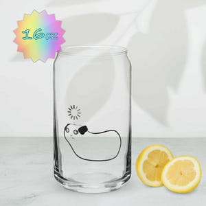 May include: A clear glass can-shaped drinking glass with a black cartoon illustration and the text "16oz" on a colorful starburst. Two lemon halves are next to the glass.