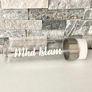 May include: Clear plastic water bottle with a white lid and a silver metal band. The bottle has the name "Mhd Islam" printed on it in white.