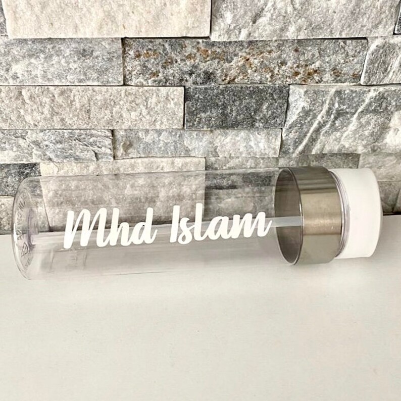 May include: Clear plastic water bottle with a white lid and a silver metal band. The bottle has the name "Mhd Islam" printed on it in white.