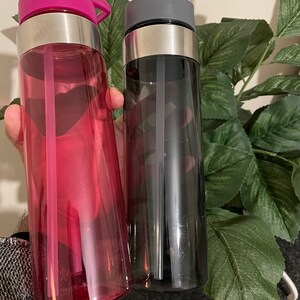 May include: Two reusable water bottles with built-in straws. One bottle is pink and the other is black.