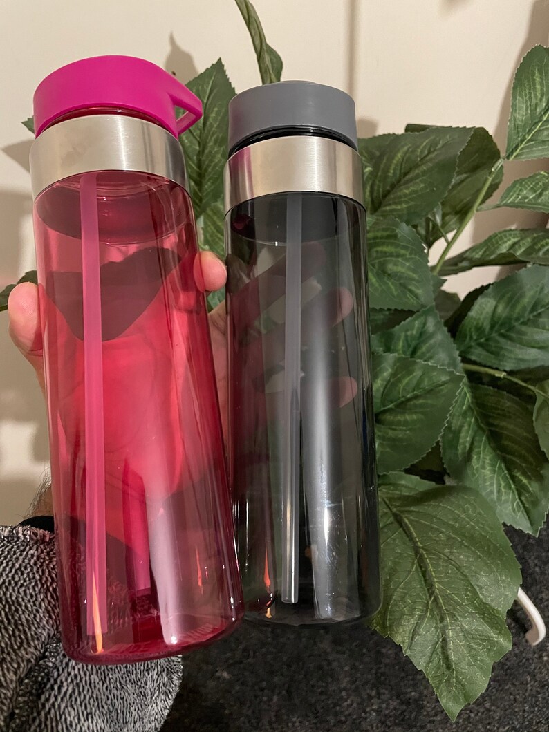 May include: Two reusable water bottles with built-in straws. One bottle is pink and the other is black.