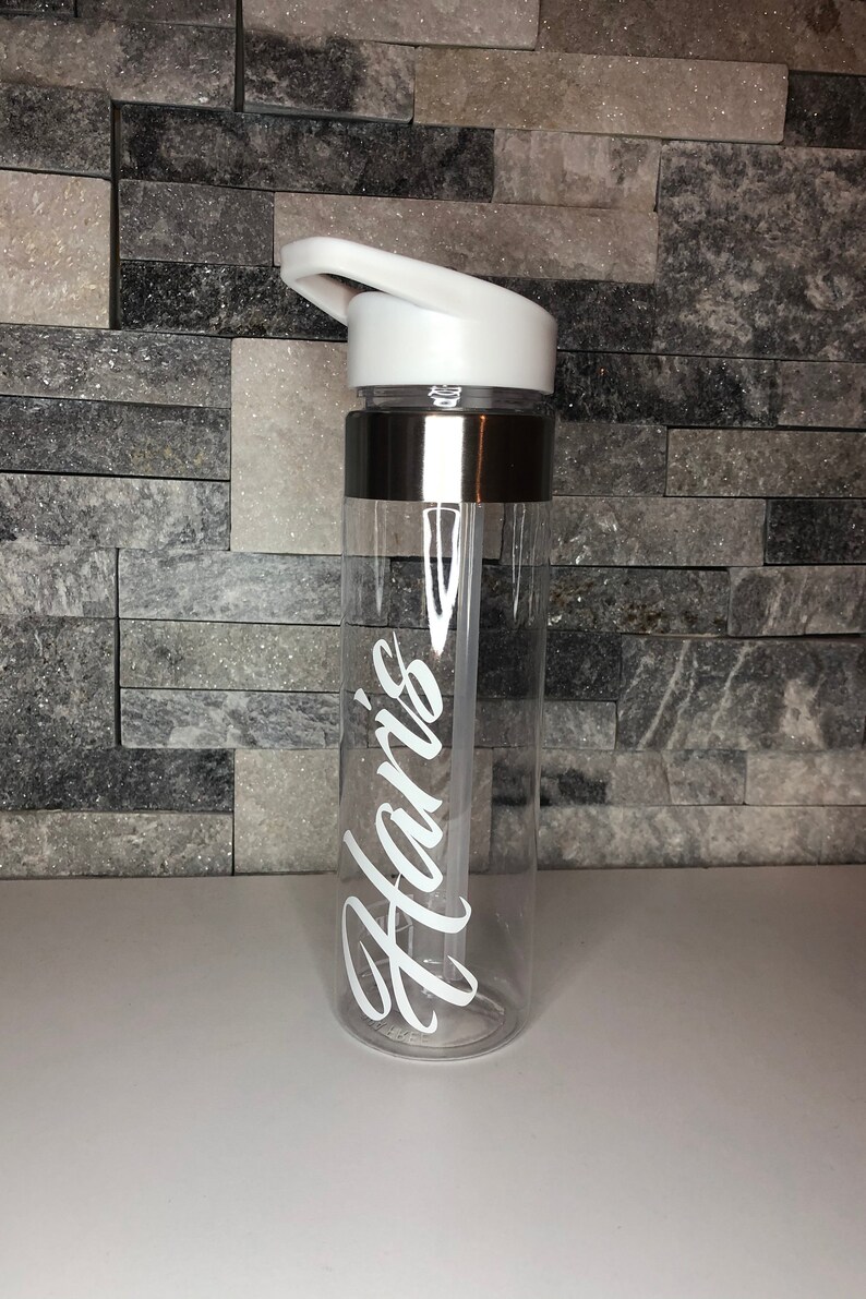 May include: A clear plastic water bottle with a white lid and a silver band around the middle. The bottle has the name "Haris" written on it in white.