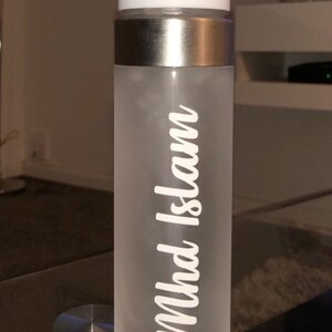 May include: A frosted white water bottle with a silver lid and a white sticker that says "Mhd Islam".