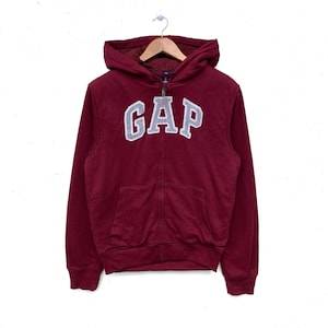 May include: A red zip-up hoodie with a gray "GAP" logo on the front. The hoodie has a fleece lining.