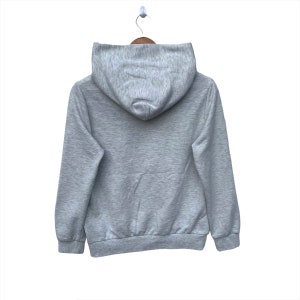 May include: A gray hooded sweatshirt with a drawstring hood. The sweatshirt has long sleeves and a kangaroo pocket.