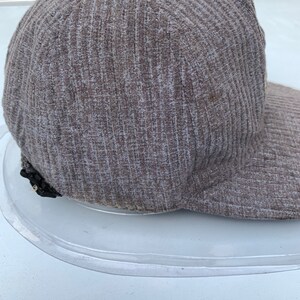 Puede incluir: Una gorra de b&eacute;isbol de color marr&oacute;n con textura de costillas y un detalle de cremallera negra en el lateral.