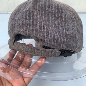 Puede incluir: Una gorra de b&eacute;isbol de color marr&oacute;n y gris con textura de costillas y una correa ajustable negra.