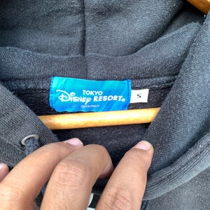 May include: A black hooded sweatshirt with a blue tag that reads "Tokyo Disney Resort" and "S" for size. The tag also has the Disney logo.