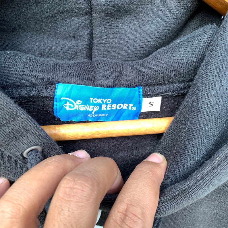 May include: A black hooded sweatshirt with a blue tag that reads "Tokyo Disney Resort" and "S" for size. The tag also has the Disney logo.