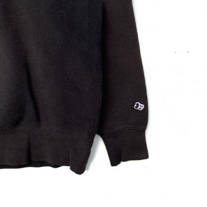 May include: Black sweatshirt with a small white embroidered logo on the left sleeve. The logo is a cartoon cloud with a face.