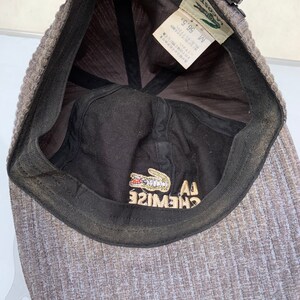 Puede incluir: Una gorra de b&eacute;isbol Lacoste gris y negra con un logotipo de cocodrilo y el texto "LA CHEMISE" en el interior. La talla es M 56,5 cm.
