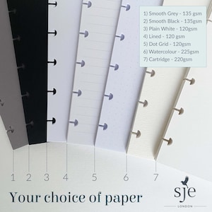 May include: Seven different paper samples for a planner or notebook. The samples are arranged from left to right, with the following colours and weights: Smooth Grey - 135 gsm, Smooth Black - 135gsm, Plain White - 120gsm, Lined - 120 gsm, Dot Grid - 120gsm, Watercolour - 225gsm, Cartridge - 220gsm. The text "Your choice of paper" is printed below the samples.