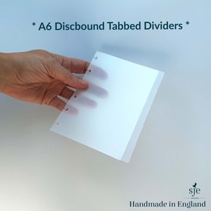 May include: A6 discbound tabbed dividers for a planner or notebook. The dividers are white and have tabs on the right side. The dividers are held in a hand.